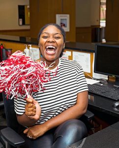 Desk assistant at building front desk waving football shaker.